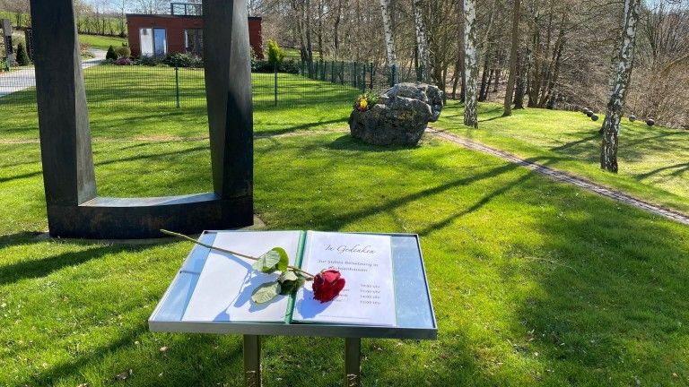 Ein Buch mit einer Rose steht auf einem Pult auf einem Friedhof